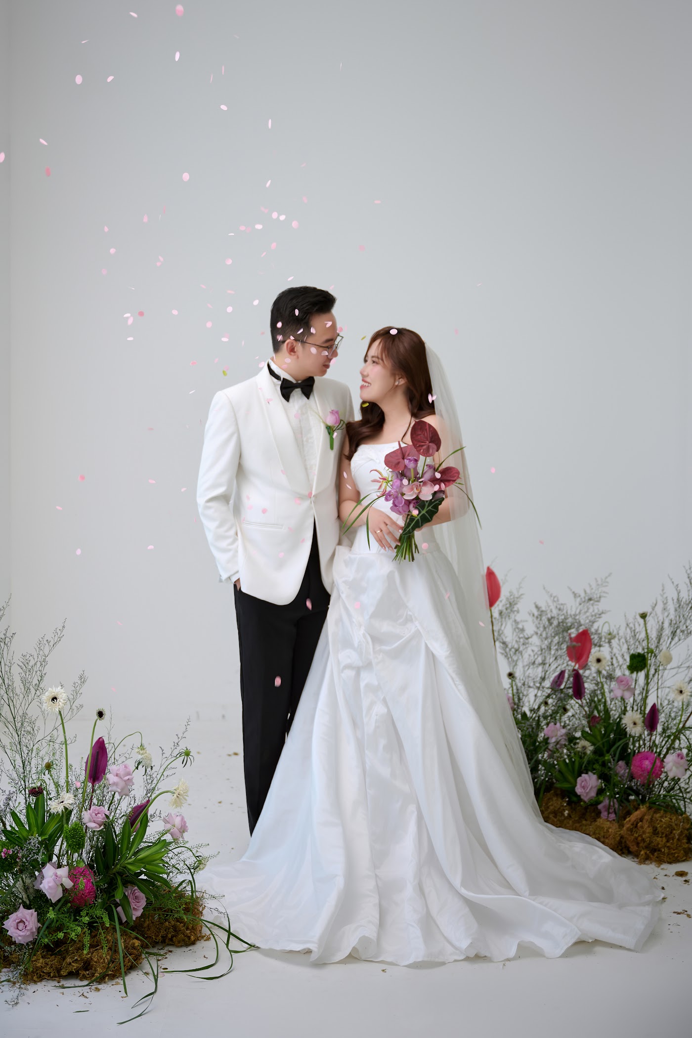 Ảnh studio: cô dâu chú rể đứng cạnh nhau bên hoa